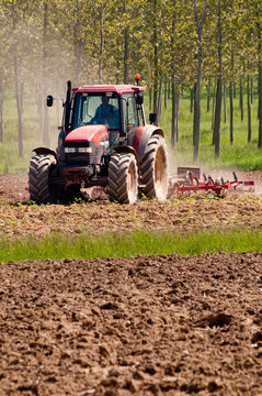 Red tractor plowing the lands background trees