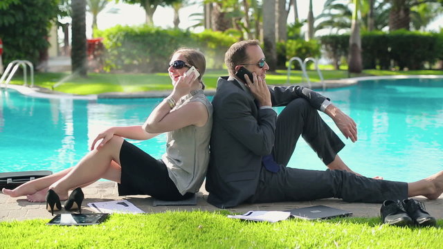 Happy business couple sitting by the poolside with cellphones