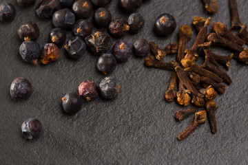 cloves and juniper berries spices on black slate stone