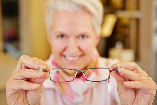 Seniorin hält Brille beim Optiker