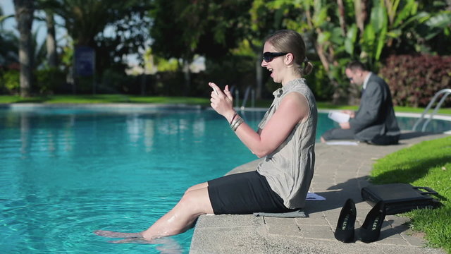 Businesswoman sitting by the poolside with cellphone