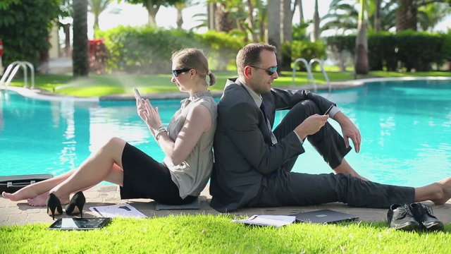 Happy business couple sitting by the poolside with cellphones