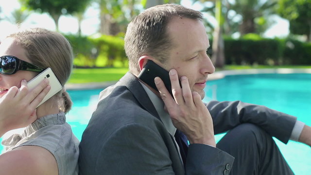 Happy business couple sitting by the poolside with cellphones