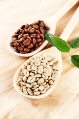 Green  and brown coffee beans in spoons and leaves