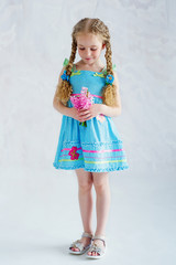 Adorable girl in blue dress holding delicate pink flowers