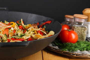 Noodles with vegetables on wok on wooden background
