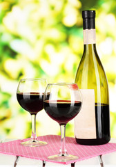Two glasses of wine and bottle on table on nature background