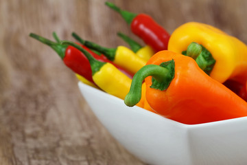 Mixed peppers and chilis in white bowl on wooden background
