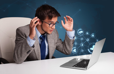 Young man sitting at desk and typing on laptop with social netwo