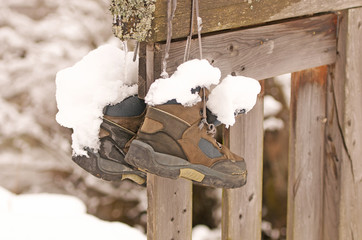 a pair of snow-covered hiking boots hanging on a wooden fence
