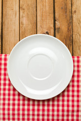 Empty plate on tablecloth over wooden background