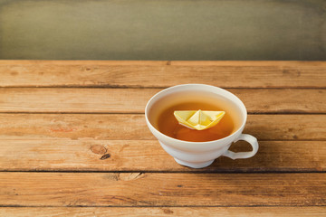 Tea cup with paper origami boat over wooden table