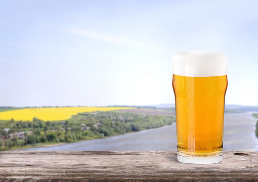 Frosty glass of light beer  with summer scene background