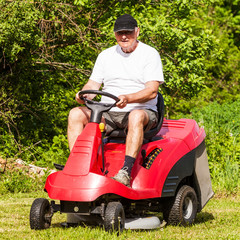 Fototapeta premium Senior man driving a red lawn mower (tractor)