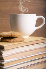 A hot cup of coffee and cookies on a stack of books