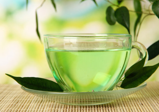 Transparent cup of green tea on bamboo mat, on nature