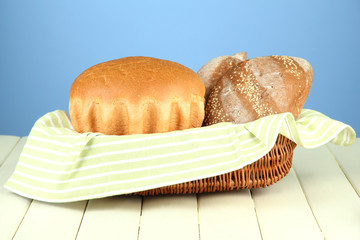 Bread in wicker basket, on wooden table, on color background