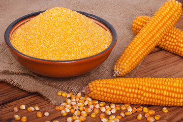 Corn groats in a bowl, whole grain and cob on a wooden table.
