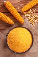 Corn groats in a bowl, whole grain and cob on a wooden table.