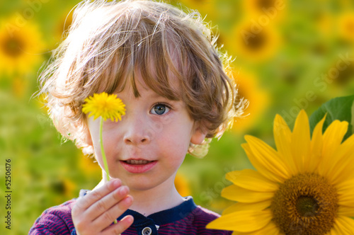 Kind mit Löwenzahn auf einem Sonnenblumenfeld