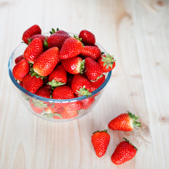 Strawberries in a glass bowl on a wooden table, square