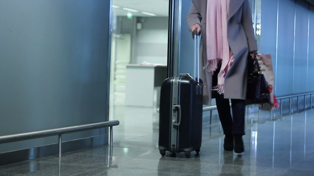 Woman with travel wheel bag coming out of airport arrival zone