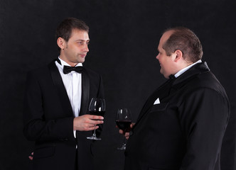 Two stylish businessman in tuxedos with glasses of red wine