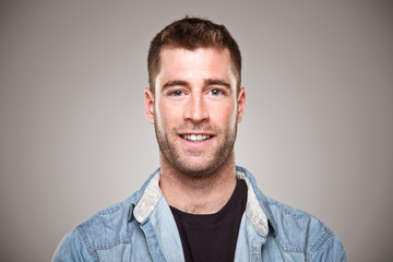 Portrait of a normal young man smiling over grey background.