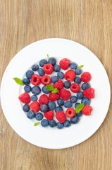Fresh raspberries and blueberries on a plate on a wooden table