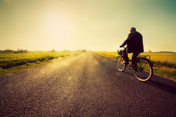 Old man riding a bike to sunny sunset sky