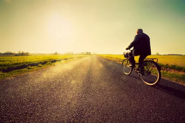 Foto auf Leinwand Alter Mann, der mit dem Fahrrad zum sonnigen Sonnenuntergangshimmel fährt © Photocreo Bednarek