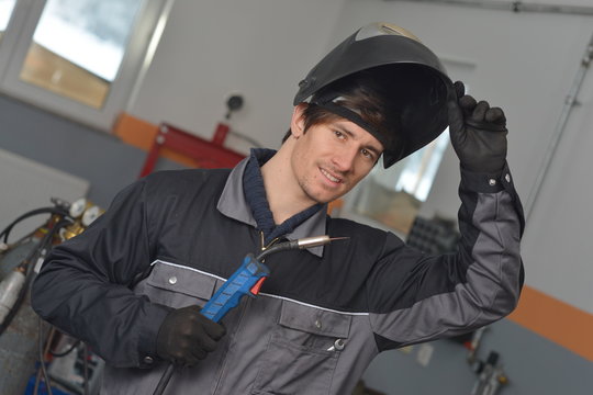Smiling welder in gray work wear and helmet at work place