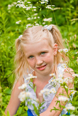 Blonde girl with two tails, sitting in the green grass with flow