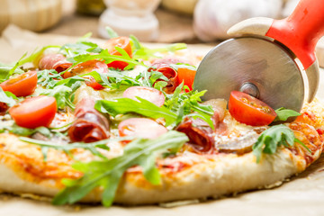 Cutting baked pizza with tomatoes and ham