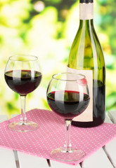 Two glasses of wine and bottle on table on nature background