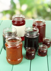 Tasty jam in banks on table on bright background