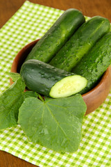 Tasty green cucumbers on color napkin, on wooden background