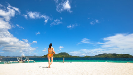 Fototapeta na wymiar young bikini girl holds a coconut standing on white beach