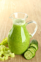 Glass pitcher of green vegetable juice on wooden background