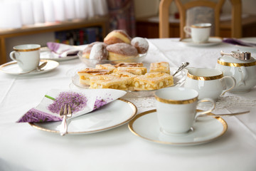 Table with coffe or tea cups, cake, plates and doughnuts