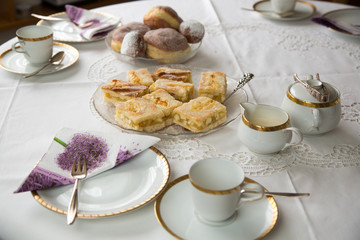 Table with coffe or tea cups, cake, plates and doughnuts