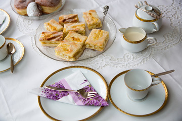 Table with coffe or tea cups, cake, plates and doughnuts