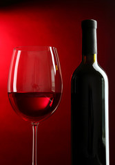 Bottle and glass of wine  on red background