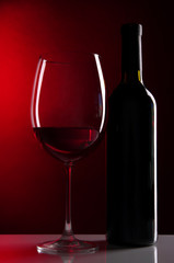 Glass of wine with bottle on bright red background