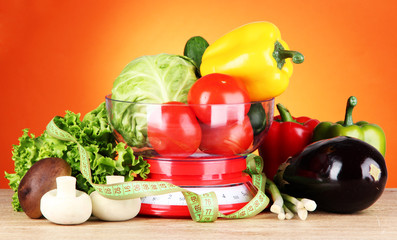 Fresh vegetables in scales on table on orange background