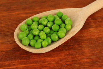 Sweet green peas in spoon on wooden background