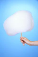 Hand holding stick with cotton candy, on color background