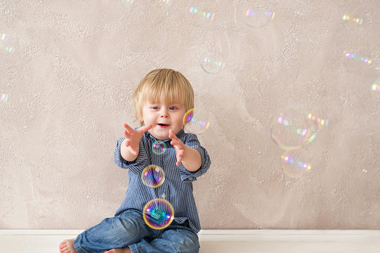 Funny little boy trying to catch colorful soap bubbles