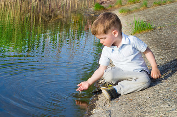 Small beautiful boy pours water from the palm on the river