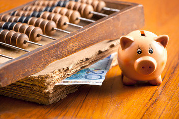 Piggy bank on a table by the old book, abacus and 20 euro bankno